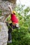 Photo of young sportsman in yellow helmet clambering over rock against background of green trees