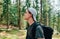 Photo of a young tourist with bristles on his face in a cap and casual clothes during a hike in a mountain sunny forest, looking