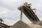 A photograph of the heavy machinery at the quarry, rocks and sand conveyor belt.