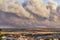 Photograph of a large forest fire with a large column of smoke on a hillside near a city