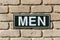 Photograph of a metal men`s toilet sign on a brick wall