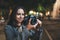 Photographer girl with retro camera take photo on background bokeh light in evening street, Blogger photoshoot concept. Tourist