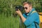 The photographer holds a professional photo-video camera in his hands. Against the backdrop of green nature and forest