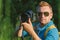 The photographer holds a professional photo-video camera in his hands. Against the backdrop of green nature and forest