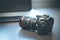 Photographer holds a reflex camera with telephoto lens in his hand. Table and laptop in the blurry background