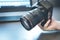 Photographer holds a reflex camera with telephoto lens in his hand. Table and laptop in the blurry background