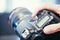 Photographer holds a reflex camera with telephoto lens in his hand. Table and laptop in the blurry background