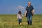 The photographer\'s grandfather walks with his little granddaughter through the field after taking a photo. They hold hands.