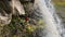 Photographer stands under a beautiful waterfall and takes pictures of nature.