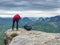 Photographer takes photos with camera on tripod on rocky mountain peak.