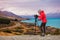 Photographer taking New Zealand travel nature photography. Woman photographer with slr camera on tripod at sunset with