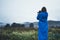 Photographer tourist in blue raincoat hold in hands photo camera take photography froggy mountains