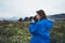 Photographer tourist girl in blue raincoat hold in female hands photo camera take photography froggy mountain, traveler shooting