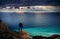 Photographer traveler stands on the edge of a cliff above the turquoise sea at sunset