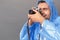 Photography Hobby. Young man in raincoat studio standing  on grey with film camera taking photos excited close