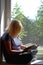 Photography of woman reading a book sitting by the window