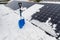 Photovoltaic panels on the roof with snow, with a snow shovel in the winter