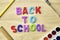 the phrase back to school is laid out in multicolored letters on the table a fountain pen a paint brush a ruler next to