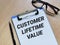 Phrase CUSTOMER LIFETIME VALUE written on paper clipboard with pen and eye glasses.