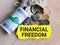 Phrase FINANCIAL FREEDOM written on strip paper with sack of coins and fake money.