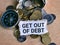 Phrase GET OUT OF DEBT written on strip paper with sack of coins and compass.