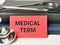 Phrase medical term written on red paper card with stethoscope and books.