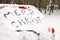 Phrase `Merry Christmas` written on snow covered car in winter forest.