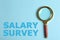 Phrase Salary Survey and magnifying glass on light blue background, top view