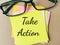 Phrase TAKE ACTION written on sticky note with eye glasses.