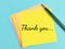 Phrase THANK YOU written on sticky note with a pen.