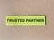 Phrase TRUSTED PARTNER written on sticky note isolated on wooden background.