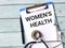 Phrase WOMEN`S HEALTH written on paper clipboard with stethoscope,syringe and a pen.