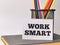 Phrase WORK SMART written on paper note with colorful pencil and a book.