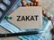Phrase ZAKAT written on label tag with money,prayer beads and calculator.