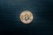 A physical bitcoin in the middle of a dark wooden background