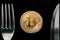Physical Golden Crytocurrency Coin between fork and knive.