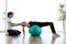 Physiotherapist helping patient to do exercise on fitness ball in physio room.