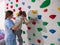 physiotherapist instructor helping little girl to climb wall in gym. sensory integration for kid and correctional