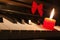 Piano keyboard with burning red candle and ribbon on it.