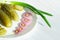 Pickled cucumbers on a white plate next to the onion rings and green onion arrow. homemade vegetables for a healthy diet. close-up