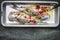 Pickled herring with herbs in bowl with marinade and fork on rustic background, top view