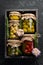 Pickled vegetables and mushrooms in glass jars in Wooden box on black stone background.