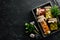 Pickled vegetables and mushrooms in glass jars in Wooden box on black stone background.