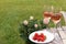 Picnic basket with glasses of delicious rose wine, strawberries and flowers outdoors, space for text