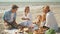 Picnic beach party friends enjoying casual conversation, drinking wine and tasting meal