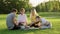 Picnic, group of four teens sitting on lawn on grass in park, eating, drinking, talking, having fun