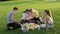 Picnic, group of four teens sitting on lawn on grass in park, eating, drinking, talking, having fun
