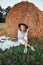 Picnic at the hayloft. Woman in cowboy hat sitting near a straw bale. Summer, beauty, fashion, glamour, lifestyle concept.