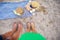 Picnic near the sea. A blue plaid on which are glasses with coffee, a bag, a hat. Feet of a couple in love. View from above