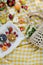 Picnic at the park. Fresh fruits and tarts on a white wooden tray, straw bag with white chamomiles